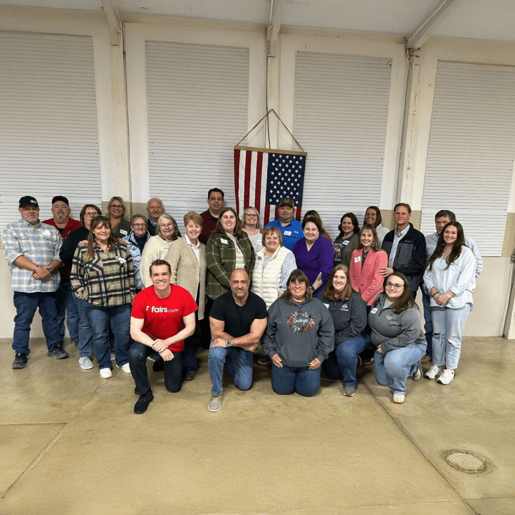 Group of people standing and kneeling indoors in front of an American flag during a team appreciation event