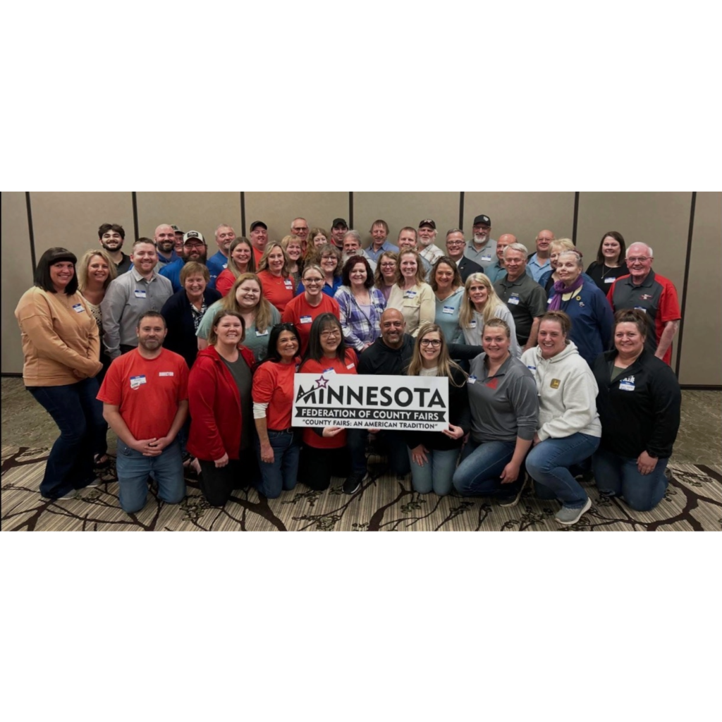 Group of Minnesota county fair leaders and community partners standing indoors and holding a sign that reads “Minnesota Federation of County Fairs – County Fairs: An American Tradition.”